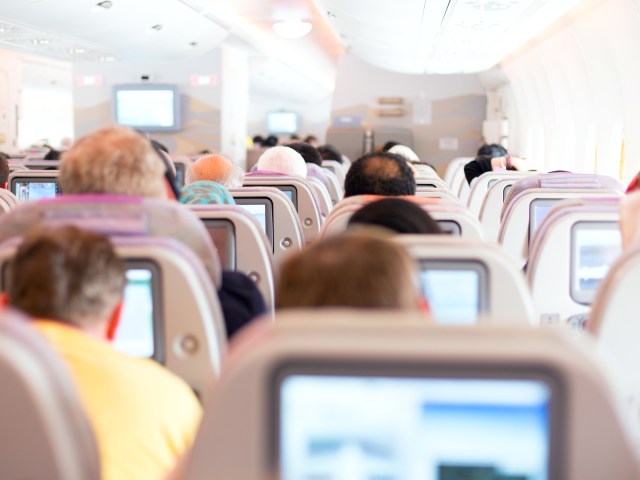 View of seatback entertainment screens and passengers in seats from rear of airplane cabin