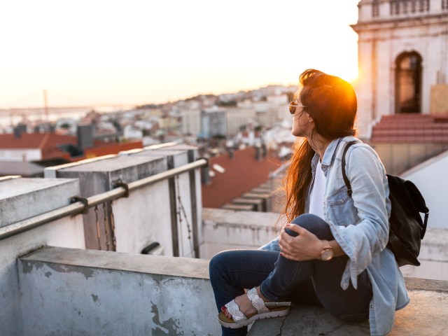 Traveler sitting on wall looking out over city at sunset