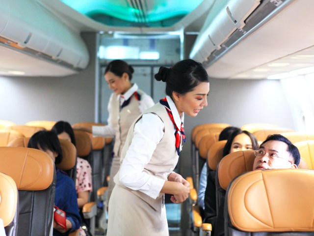 Flight attendants in aircraft aisle speaking to passengers