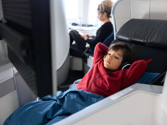 Child reclining in airplane seat watching in-flight entertainment screen