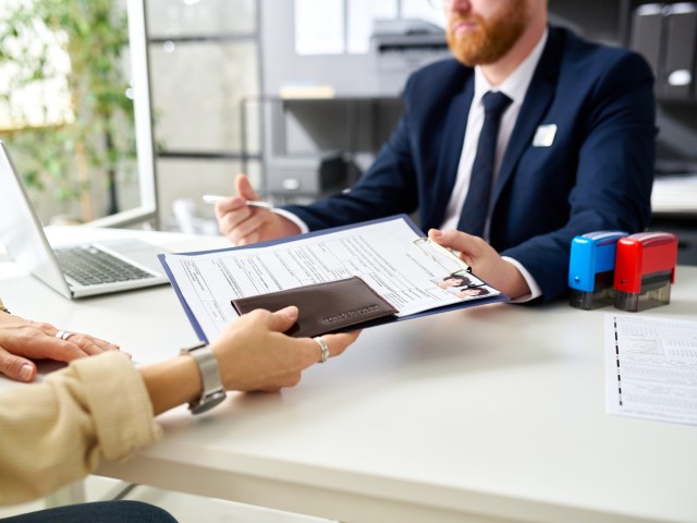 Person handing passport application to official at desk