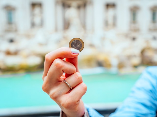 Person holding 1 euro coin in front of Trevi Fountain