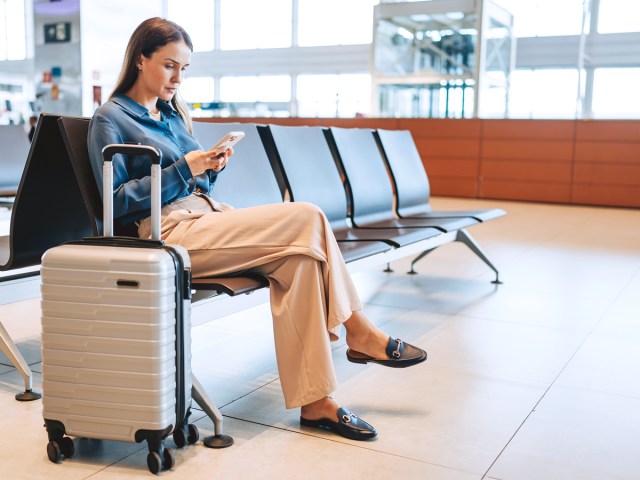 Airline passenger sitting in terminal using cellphone