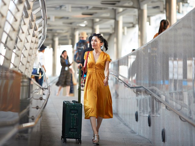 Woman in dress rolling suitcase through airport