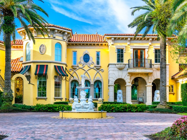 Bright yellow Mediterranean-style mansion with fountain and palm trees in Florida