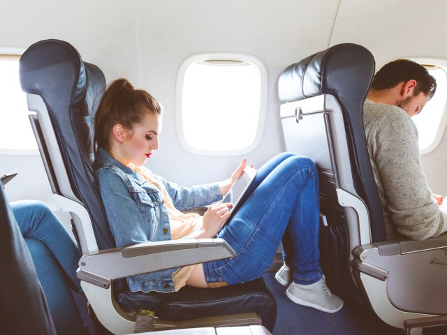 Airline passenger reading book and resting knees on seatback in front