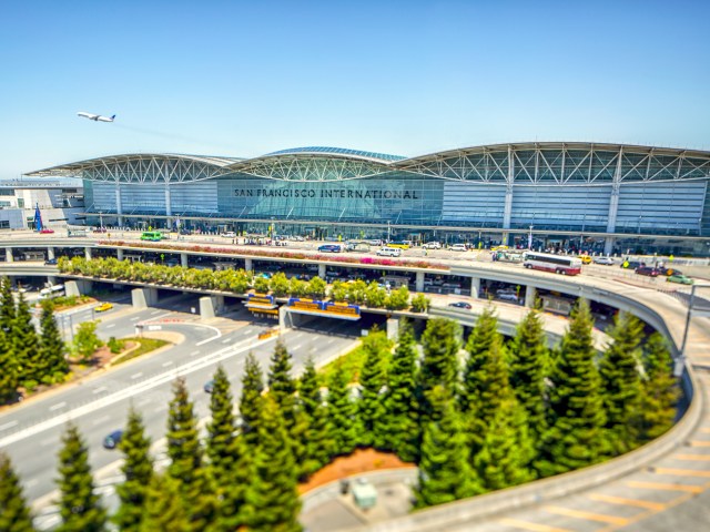 Jet taking off in distance with sweeping glass facade of the International Terminal in foreground at San Francisco International Airport