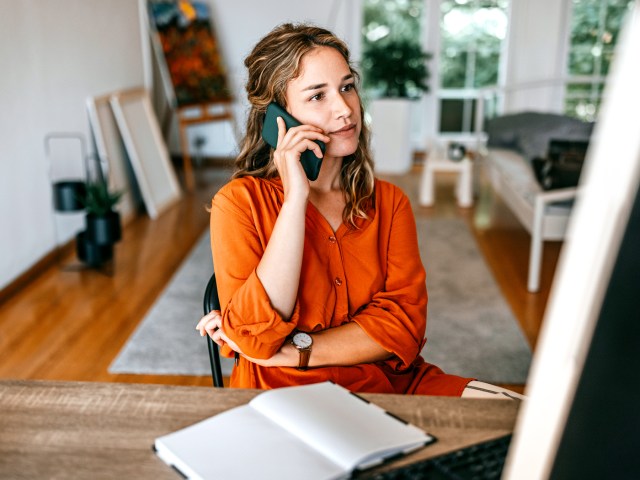 Woman talking on phone and sitting at desk with notepad