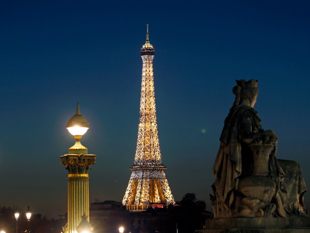 Statue and lamppost framing the Eiffel Tower in Paris lit at night