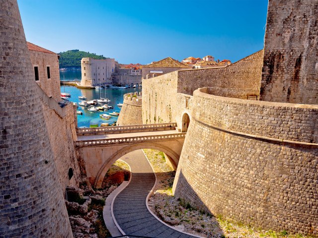 A peek between two sections of stone walls, through which you can see blue ocean