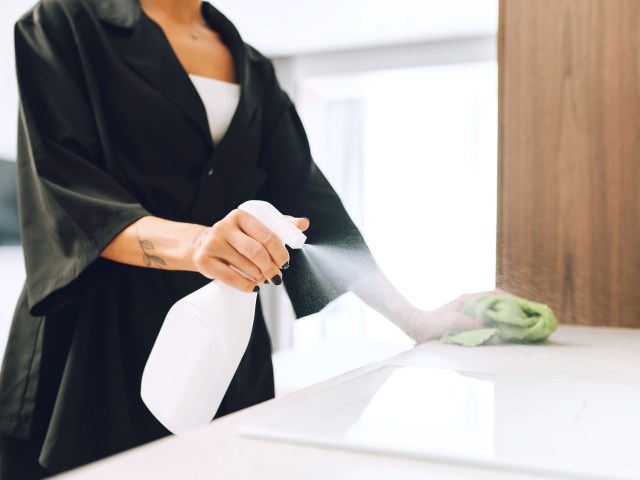 Person cleaning countertop with spray and rag