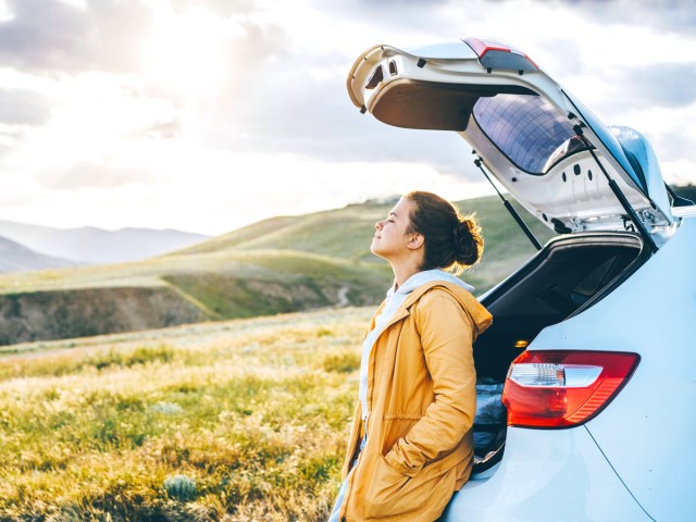 Traveler leaning back on car overlooking countryside