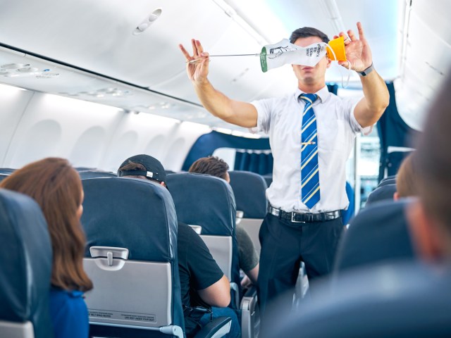 Flight attendant performing safety demonstration in aircraft aisle