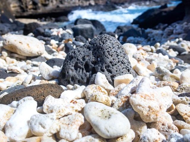 Close-up view of lava rock on beach with waves in background