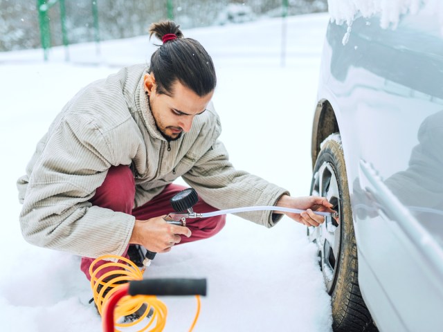 Man checking tire pressure in snow