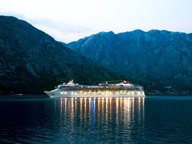 Cruise ship illuminated at dusk, surrounded by coastal mountains