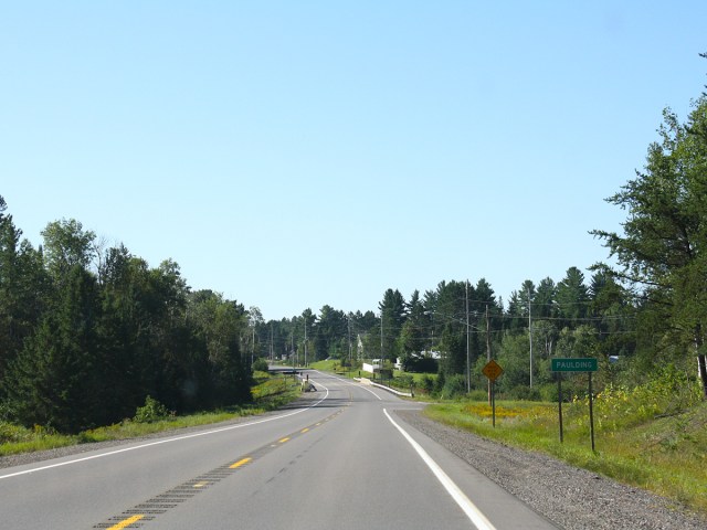 Empty two-lane highway with sign for town of Paulding, Michigan