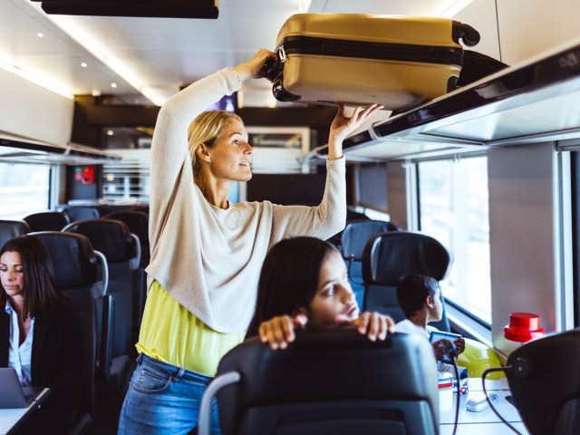 Rail passenger placing suitcase on overhead rack