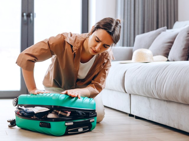 Person trying to pack overstuffed suitcase