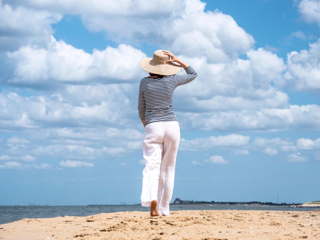 Woman holding hat and walking on sandy beach