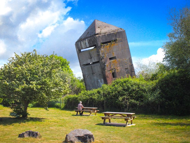 Man sitting at picnic table in front of La Tour Penchée in Oye-Plage, France