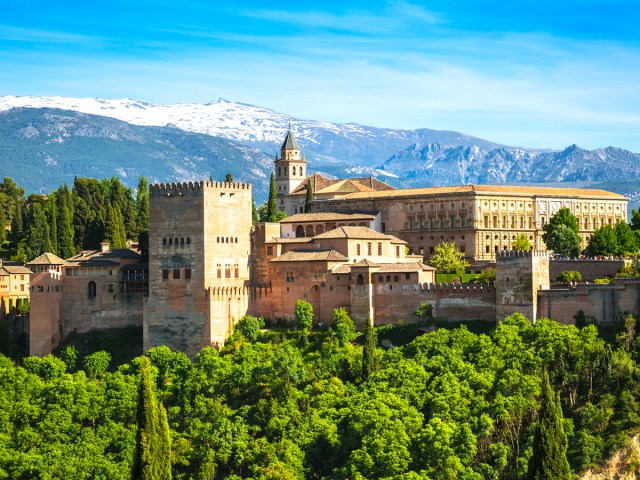 Spain's Alhambra Palace, seen above tree tops with snow-capped mountains in background