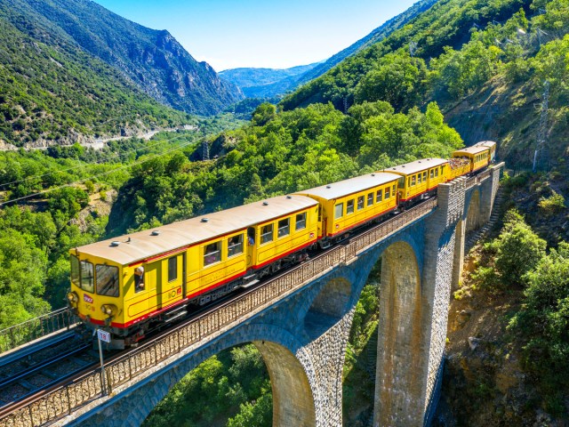 Le Petit Train Jaune traversing stone arch bridge over valley in France