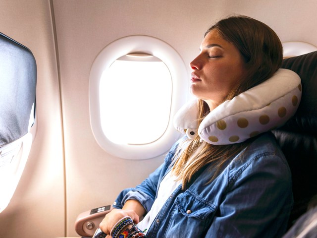 Airline passenger in window seat using neck pillow to sleep