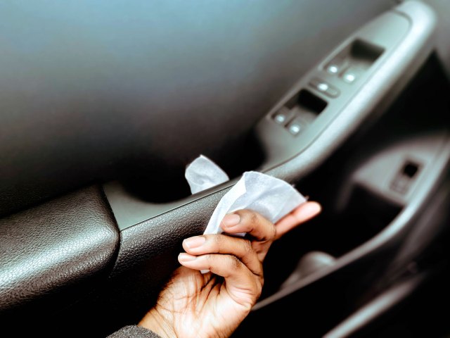 Person cleaning car door handle with wipe