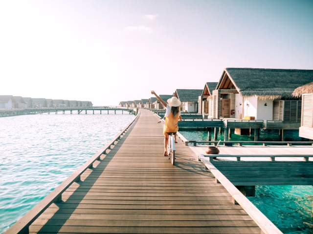 Resort guest riding bike on walkway leading to overwater bungalows