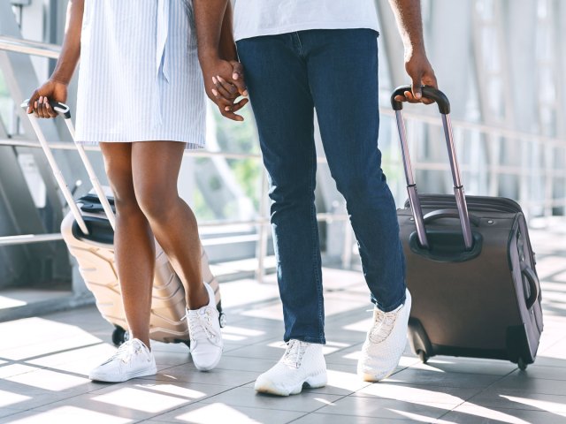 Couple holding hands and rolling luggage through airport terminal