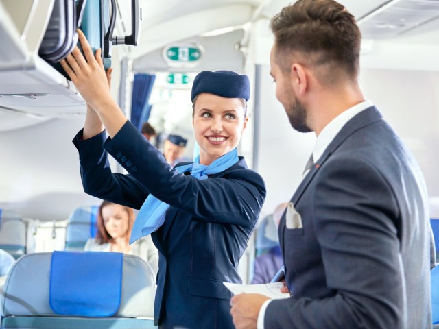 Flight attendants talking in aisle and placing bags in overhead bin