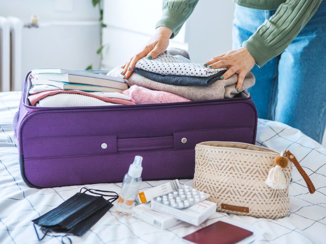 Person packing items in suitcase on bed