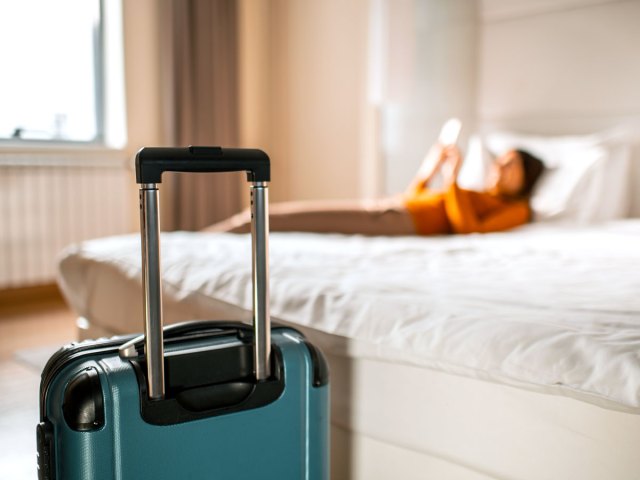 Person lying on bed next to suitcase