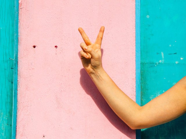 Person giving peace sign against pink wall