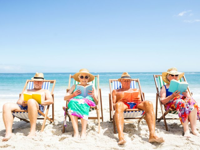 Group sitting on beach in lounge chairs reading books