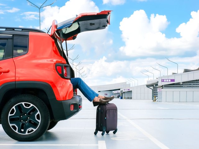Person sitting in car trunk resting feet on suitcase