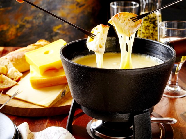 Diners dipping bread into pot of cheese fondue