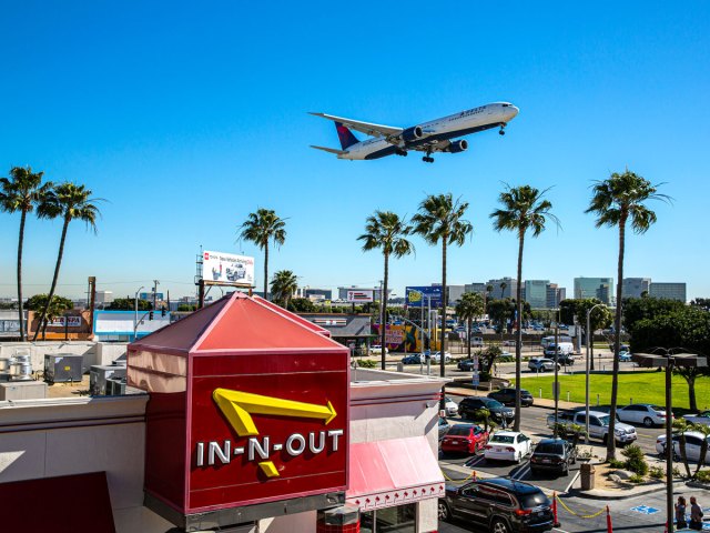 Aircraft landing over palm trees and In-n-Out burger location beside Los Angeles International Airport