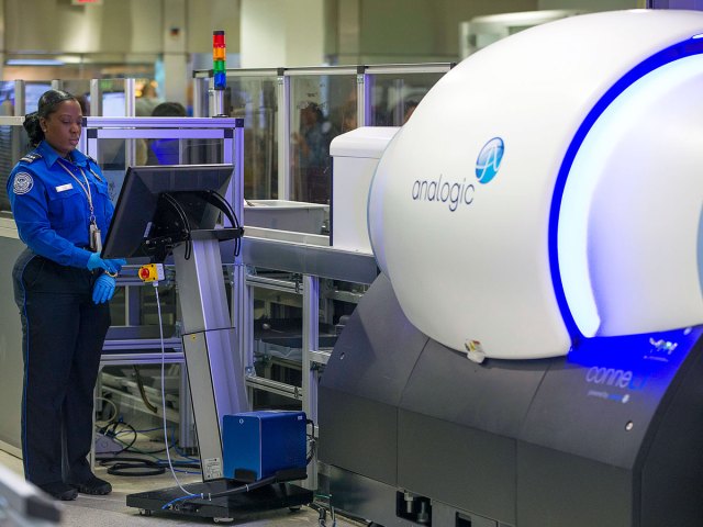 TSA officer reviewing X-ray scans of bags at security checkpoint with new CT scanner