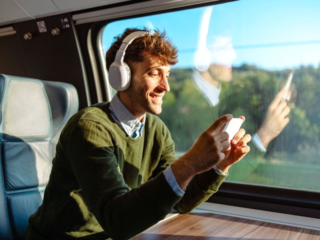 Man using headphones to watch video on phone while riding train