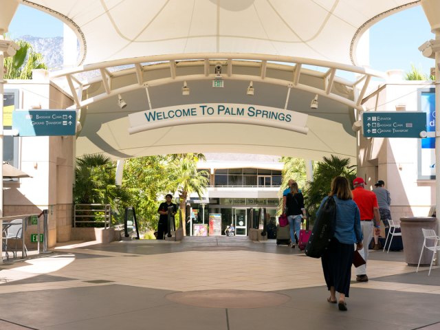 Passenger walking through outdoor area under "Welcome to Palm Springs" sign at Palm Springs International Airport