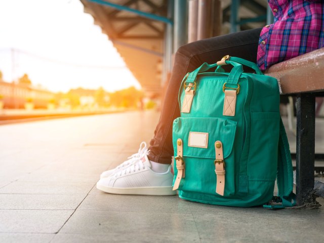 Traveler sitting on train platform bench with backpack on ground